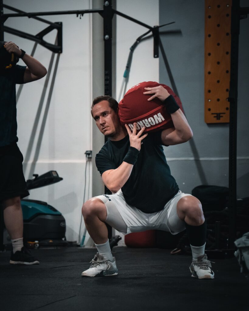 Člen CrossFit Senec robí drep so strongman vrecom na pleci