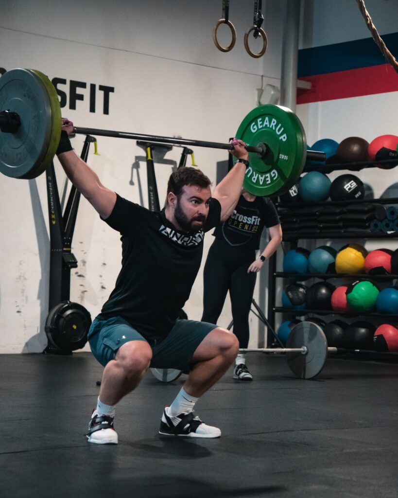 Člen CrossFit Senec v podrepe s činkou nad hlavou pri trhu
